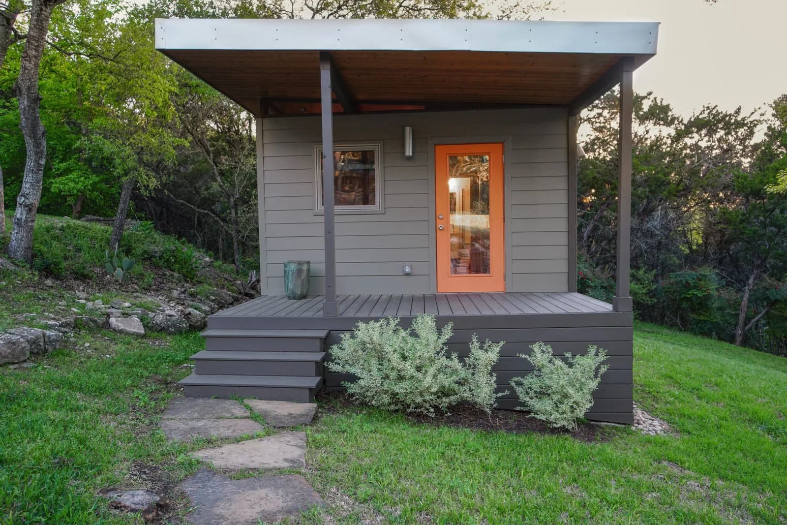 Kanga Modern studio with covered porch, orange glass door and painted lap siding on a sloped lot
