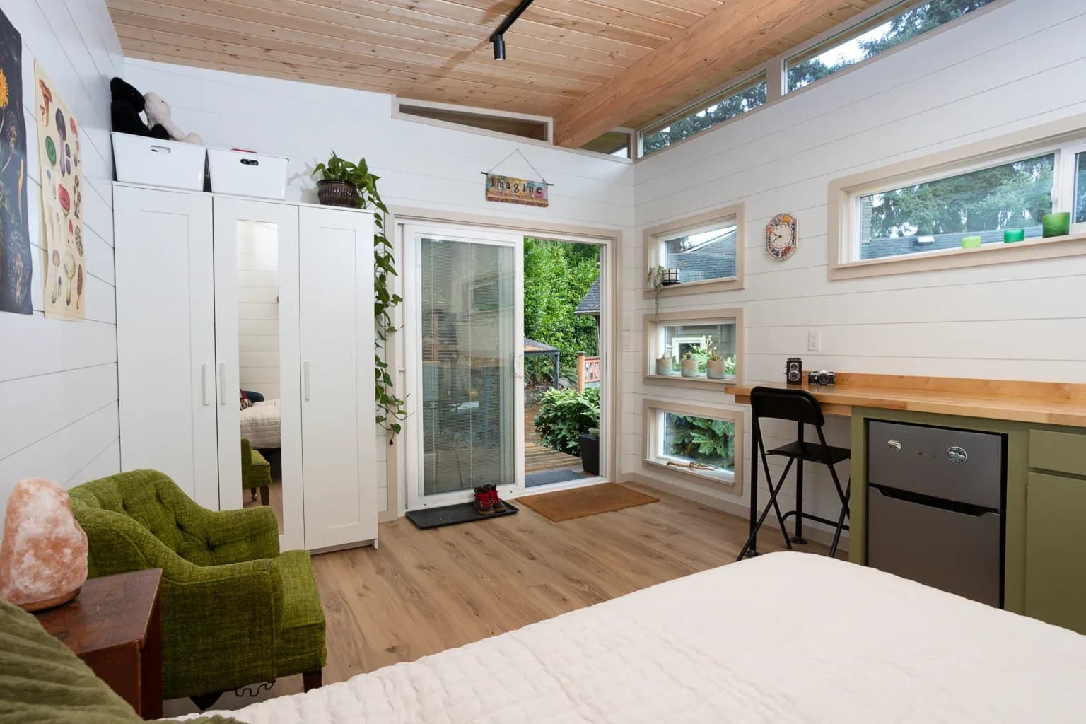 Modern Shed guest suite interior with bed, desk counter, mini fridge, and sliding glass door to a deck