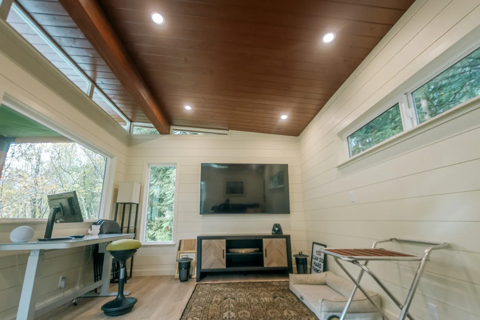 Modern Shed interior with standing desk, wall-mounted TV, shiplap walls, and stained wood ceiling