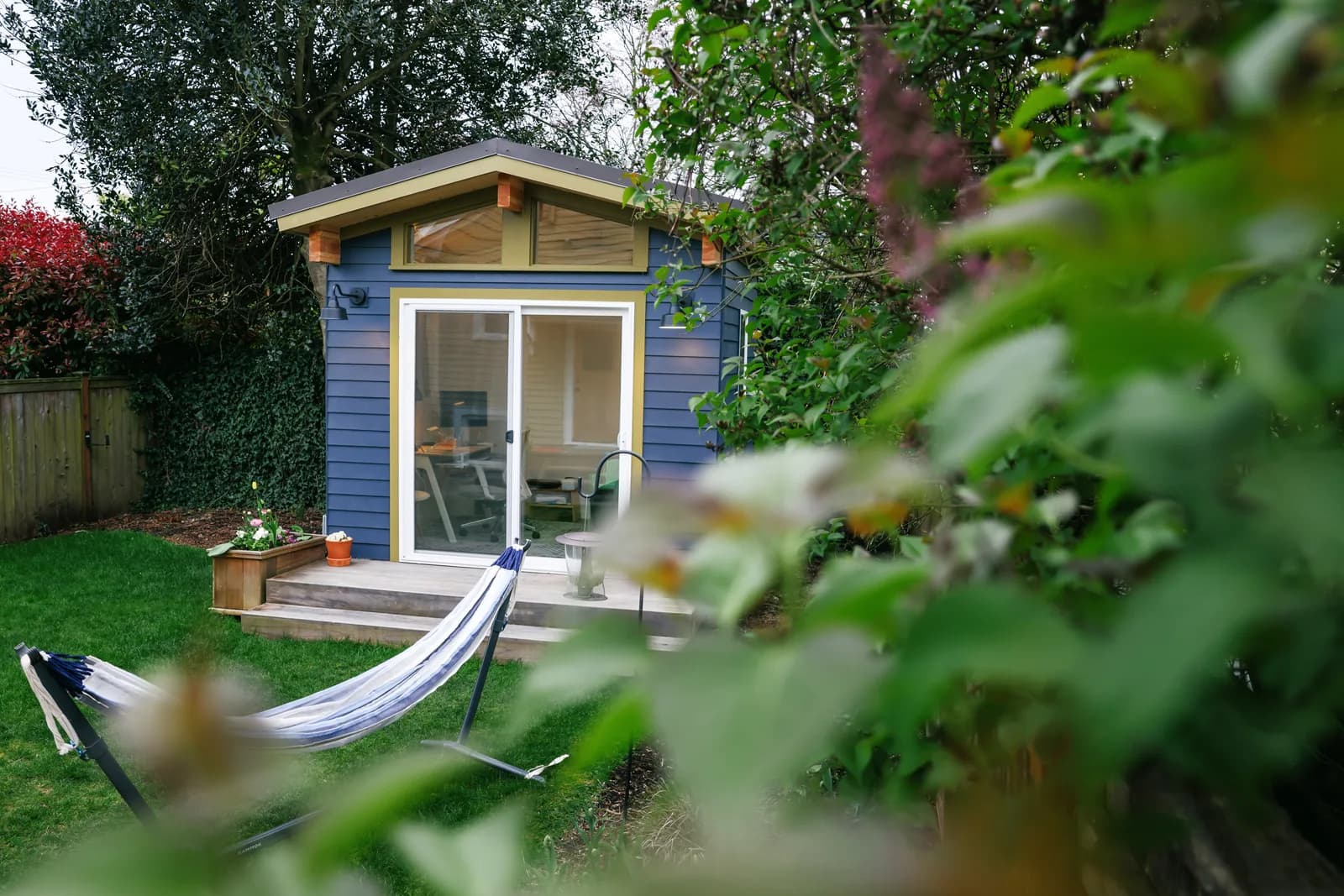 Blue gable-roof Modern Shed backyard office with sliding glass door and desk visible inside
