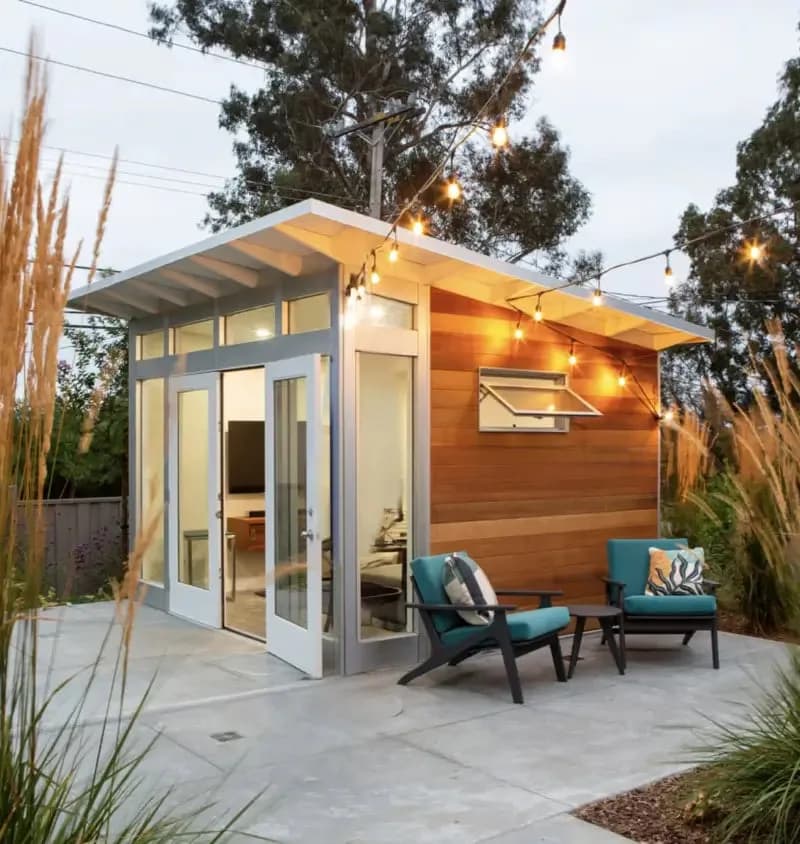 Studio Home Signature studio with cedar siding and transom windows under string lights at dusk